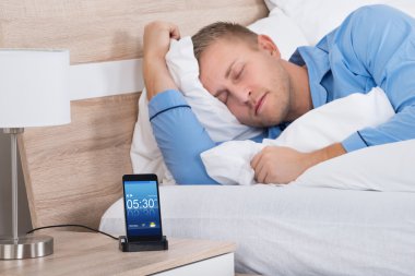 Alarm ile cep telefonu üzerinde uyuyan adam