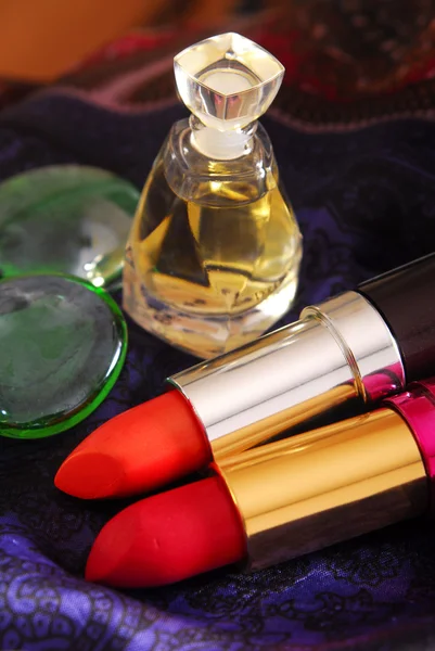 Lippenstiften en parfum op donkere zijdeachtige sjaal — Stockfoto