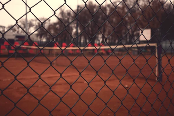 View on empty tennis yard through fence.