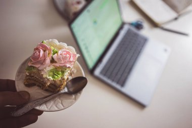 Tepside bir parça doğum günü pastası, arkada bir dizüstü bilgisayar..