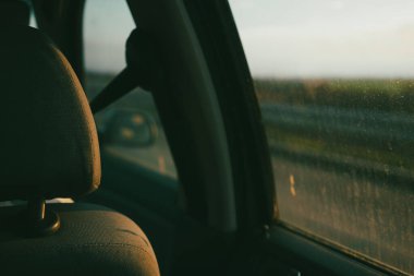 Kirli bir pencereden bir arabanın arka koltuğundan, cam parçalarından ve bulanık doğa arka planından bak.