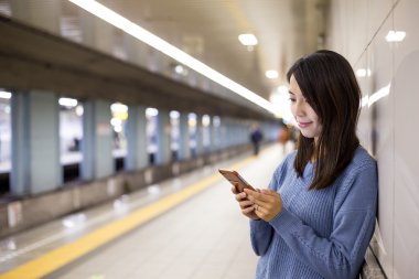Tren platformu üzerinde akıllı telefon kullanan kadın