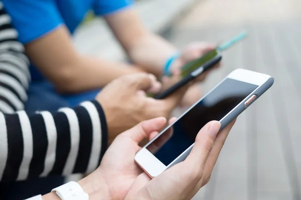 Pessoas usando celular juntos e sentados ao ar livre — Fotografia de Stock