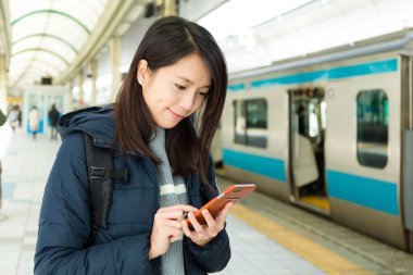 Tren platformu üzerinde cep telefonu kullanan kadın