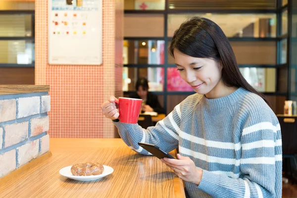 Женщина с мобильным телефоном наслаждается кофе — стоковое фото