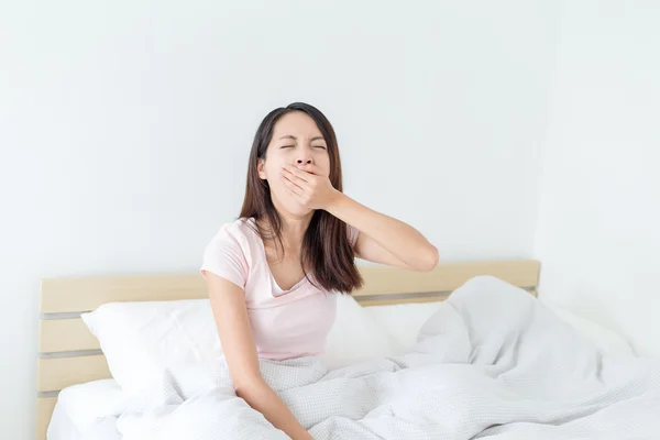 Woman yawning and sitting on bed — Stock Photo, Image