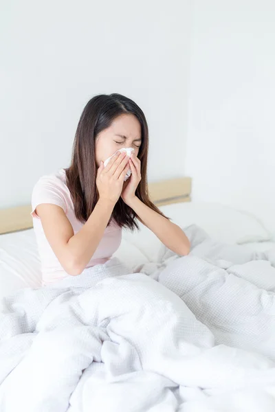 Woman sneezing and sitting on bed — Stock Photo, Image