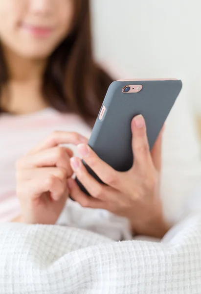 Wanita menggunakan ponsel dan duduk di tempat tidur — Stok Foto