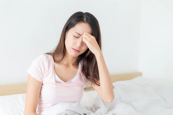 Женщина чувствует головную боль и сидя на кровати — стоковое фото