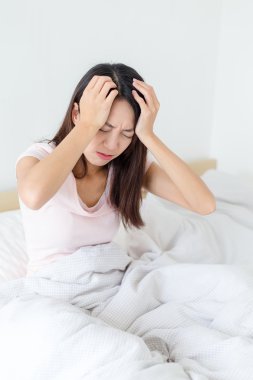 Kadın yatağında oturup baş ağrısı ile 