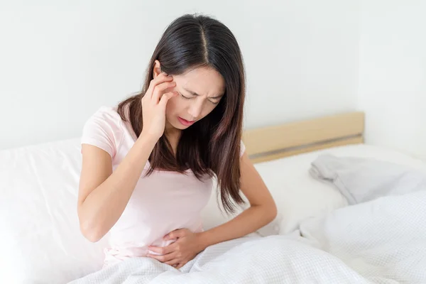 Wanita duduk di tempat tidur dengan rasa sakit — Stok Foto