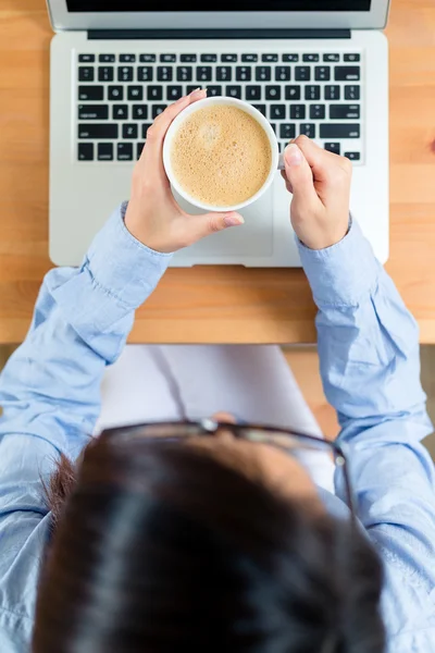 Mujer sosteniendo con taza de café y el uso de ordenador portátil — Foto de Stock