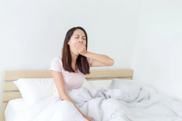 Женщина сидит на кровати и зевает — стоковое фото