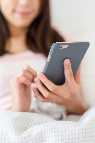 Frau liegt im Bett und hält Handy in der Hand — Stockfoto