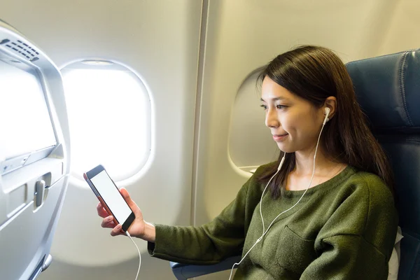 Donna che ascolta musica con cellulare in aereo — Foto Stock