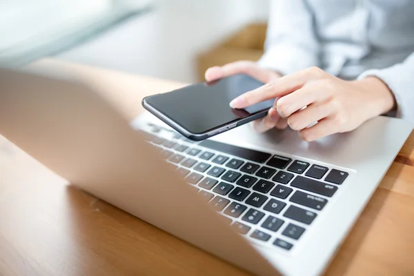 Woman hand touch phone over laptop keyboard — Stock Photo, Image