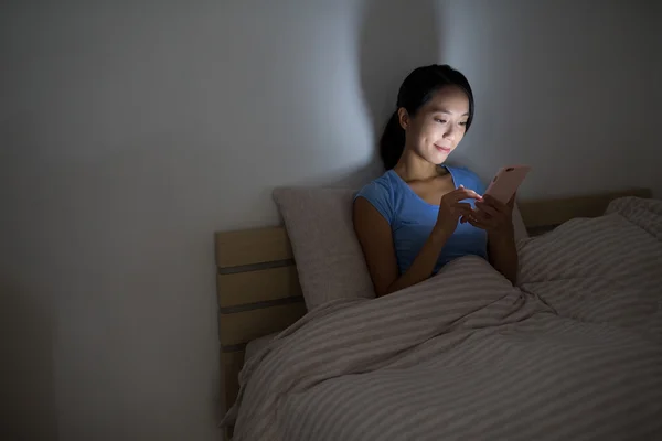 Wanita menggunakan ponsel dan duduk di tempat tidur — Stok Foto