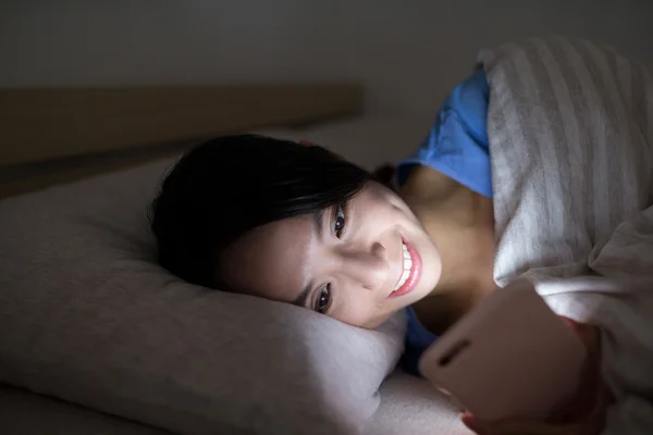 Femme utilisant un téléphone portable et couchée au lit — Photo