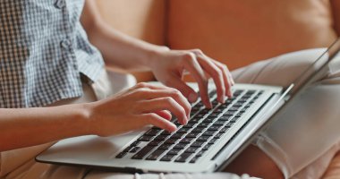 Kadın dizüstü bilgisayarda çalışıyor ve kanepeye oturuyor.