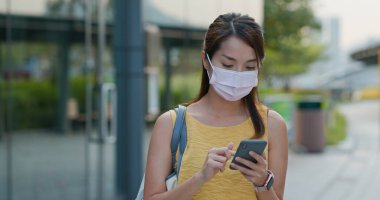 Kadın yüz maskesi takıyor ve şehirde akıllı telefon kullanıyor.