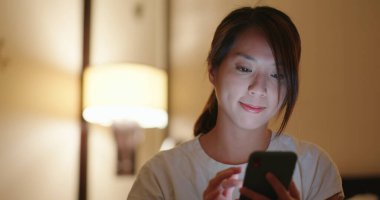 Kadın cep telefonu kullanıyor ve geceleri yatakta oturuyor.
