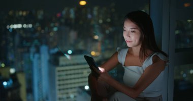 Kadın akıllı telefon kullanıyor, cep telefonu kullanıyor ve pencere kenarına oturuyor