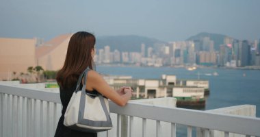 Kadın yüz maskesi takıyor ve şehir manzarasına bakıyor.