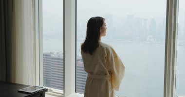 Sabahları pencereden manzaranın tadını çıkarmak için bornozlu kadın ve perdeyi aç.