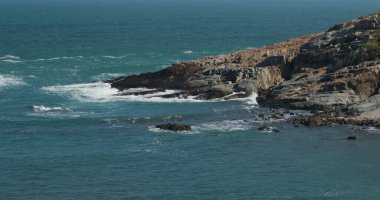 Deniz dalgaları adada kayalara çarpıyor.