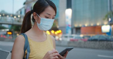 Kadın yüz maskesi takıyor ve şehirde akıllı telefon kullanıyor.