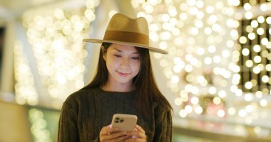 Geceleri şehirde Noel süslemeli cep telefonu kullanan kadın.