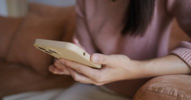 Kadın cep telefonu kullanıyor ve evdeki kanepeye oturuyor.