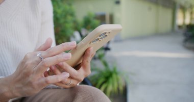 Kadın cep telefonu kullanıyor ve parkta oturuyor.