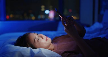 Kadın cep telefonu kullanıyor ve geceleri yatağa uzanıyor.