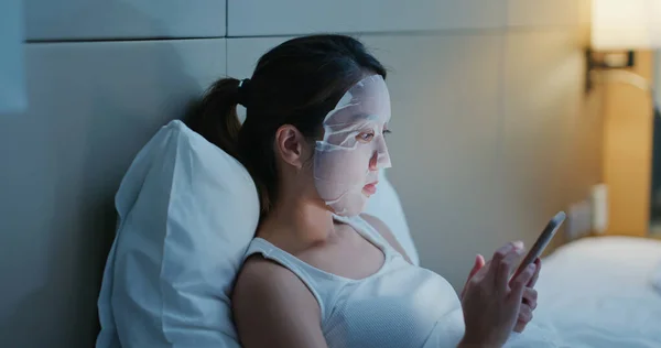Vrouw Aanbrengen Gezichtsmasker Gebruik Van Mobiele Telefoon Bed Nachts — Stockfoto