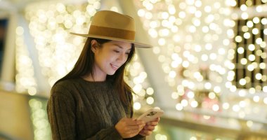 Geceleri şehirde Noel süslemeli cep telefonu kullanan kadın.