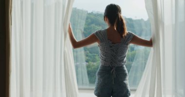 Kadın odanın perdesini aç.