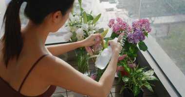 Balkonda çiçeğini sulayan bir kadın.