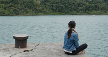 Kadın rıhtımda oturur ve deniz manzarasının tadını çıkarır.