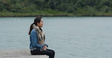 Kadın iskelede oturuyor ve manzaranın tadını çıkarıyor.