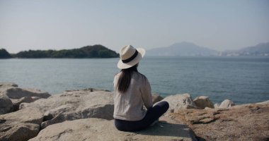 Kadın deniz kenarında oturur ve manzaraya bakar.