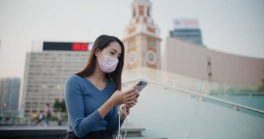 Kadın yüz maskesi takıyor ve dışarıda cep telefonu kullanıyor.