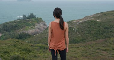 Kadın dağın tepesinde durur ve manzaranın tadını çıkarır.