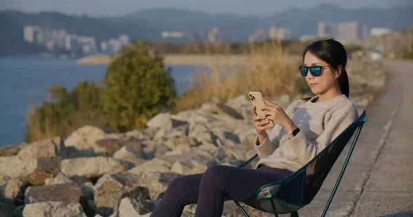 Kobieta Nosi Okulary Przeciwsłoneczne Korzystanie Smartfona Siedzieć Fotelu Kempingowym — Zdjęcie stockowe