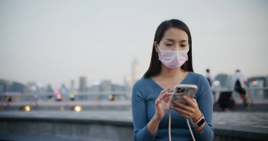 Kadın yüz maskesi takıyor ve gece akıllı telefon kullanıyor.