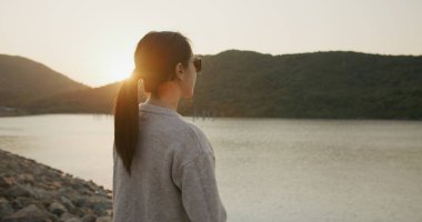 Kadın deniz kenarında gün batımına bak.