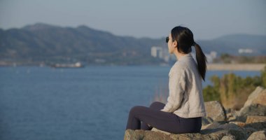 Kadın deniz kenarında oturur ve manzaraya bakar.