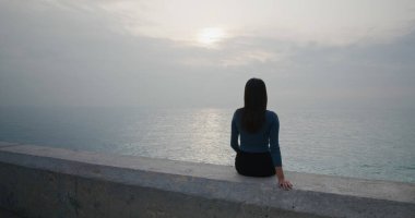 Kadınlar deniz kenarında oturur ve günbatımının tadını çıkarırlar.