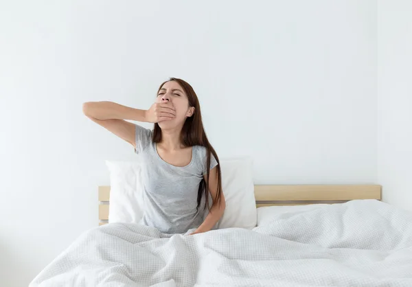 Азиатка зевает на кровати — стоковое фото