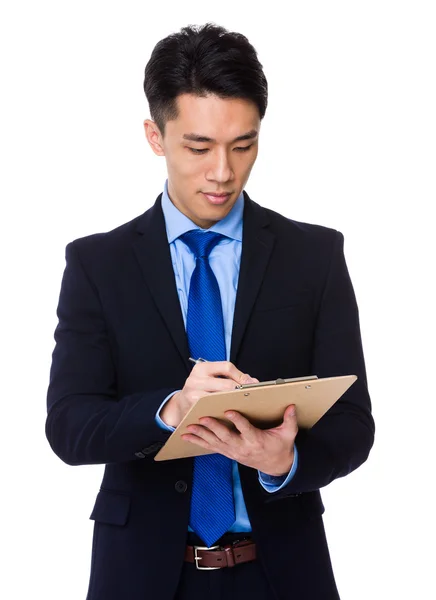 Asian businessman writing on clipboard — Stock Photo, Image